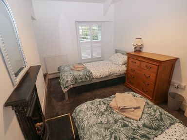 A bedroom with two single beds a wooden dresser a window with shutters and a small fireplace at Rushfield in St Dogmaels North Pembrokeshire