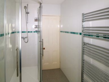 A bathroom with a glass door shower enclosure wall-mounted showerhead towel radiator and a closed door at Rushfield St Dogmaels North Pembrokeshire