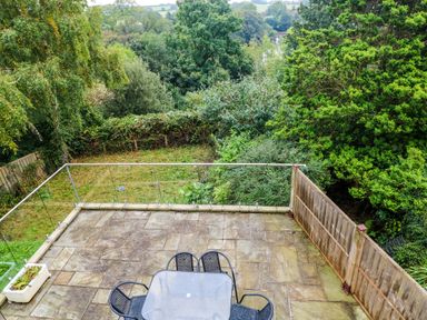 A stone patio with a glass table and four chairs overlooking a garden with trees and shrubs at Rushfield in St Dogmaels North Pembrokeshire