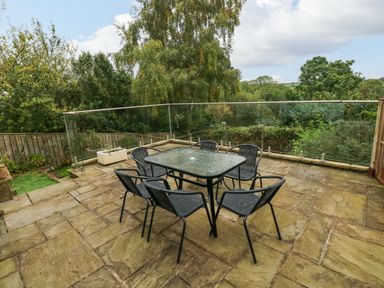 An outdoor patio with a glass table and six black chairs surrounded by glass railing at Rushfield in St Dogmaels North Pembrokeshire