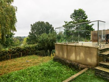 A garden area with grass and trees next to a raised patio with glass fencing at Rushfield in St Dogmaels North Pembrokeshire