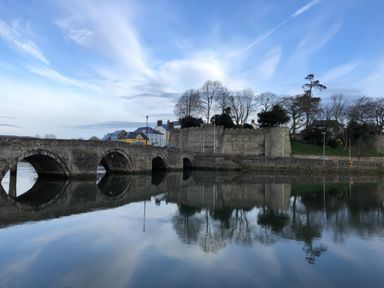 A stone bridge over calm water with a historic stone wall and buildings in the background at Rushfield in St Dogmaels North Pembrokeshire