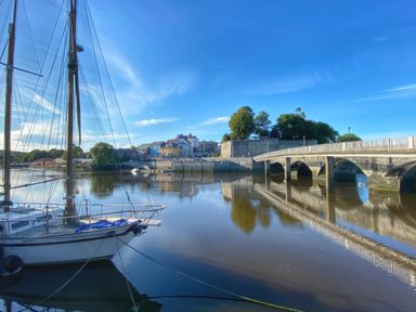 A sailboat docked on calm water near a stone bridge and buildings at Rushfield in St Dogmaels North Pembrokeshire