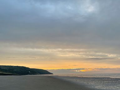 A beach with wet sand and a cloudy sky at sunset with hills in the background at Rushfield in St Dogmaels North Pembrokeshire