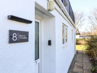 The exterior entrance of a white building with a black sign reading 8 Beachcomber and a walkway beside it at Beachcomber Maer near Bude