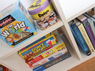 A shelf with board games and books including The World BrainBox Dobble and Dont Say It at Beachcomber Maer near Bude