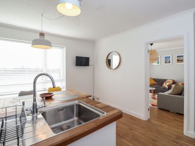 A kitchen area with a sink and wooden countertops next to a dining table with placemats and chairs at Beachcomber Maer near Bude