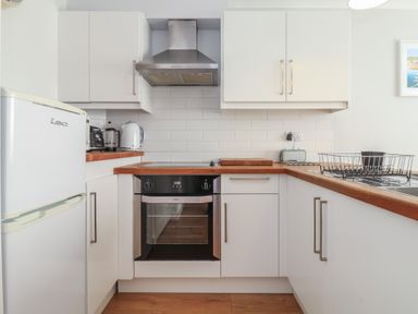 A kitchen with white cabinets wooden countertops an oven a fridge a toaster a kettle and a dish drying rack at Beachcomber in Maer near Bude