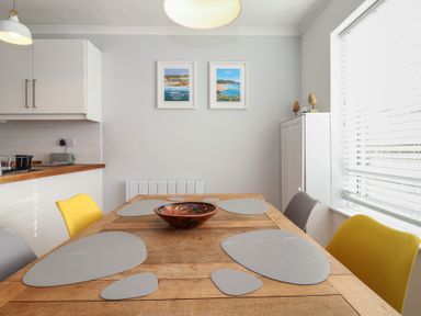 A dining area with a wooden table and mixed yellow and gray chairs at Beachcomber in Maer near Bude