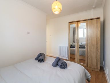 A bedroom with a bed with rolled towels and a wooden wardrobe with mirrors at Beachcomber Maer near Bude
