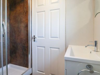 A bathroom with a shower enclosure a white door and a sink with a faucet at Beachcomber in Maer near Bude