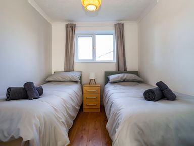 A bedroom with two single beds a nightstand with a lamp between the beds and a window with curtains at Beachcomber Maer near Bude