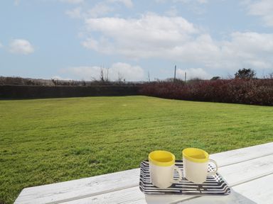 A grassy garden with two mugs on a tray on a white wooden table at Beachcomber in Maer near Bude