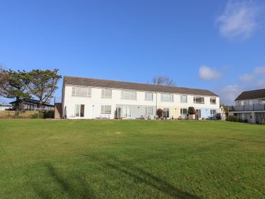 A row of connected houses with front gardens and picnic tables on a grassy lawn at Beachcomber in Maer near Bude