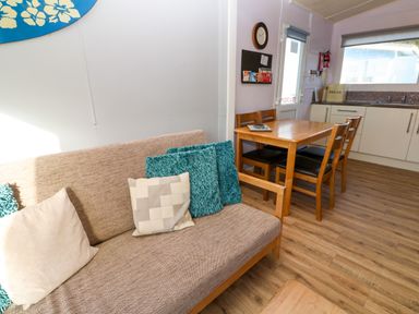 A kitchen and dining area with a wooden table and chairs and a sofa with cushions at Chalet 3 Wipeout in Hayle