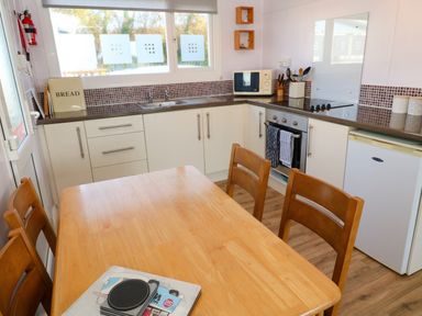 A kitchen with a wooden table and chairs a countertop with a sink microwave oven stove and refrigerator at Chalet 3 Wipeout in Hayle
