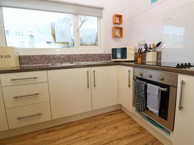 A kitchen with white cabinets a microwave oven and utensils at Chalet 3 Wipeout in Hayle