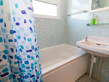 A bathroom with a bathtub a patterned shower curtain a sink and a window at Chalet 3 Wipeout in Hayle