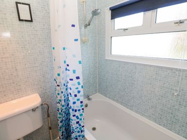 A bathroom with a bathtub shower curtain toilet and a window at Chalet 3 Wipeout in Hayle