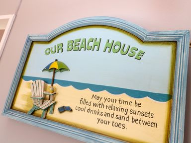 A decorative beach house sign with a chair umbrella and text about relaxing sunsets at Chalet 3 Wipeout in Hayle