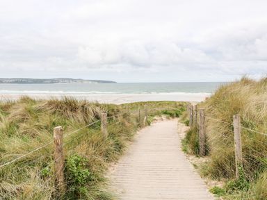 A sandy path with wooden posts and wire fencing leading through grassy dunes to a beach and sea at Chalet 3 Wipeout in Hayle