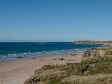 A beach with a distant lighthouse and rock formations at Chalet 3 Wipeout in Hayle