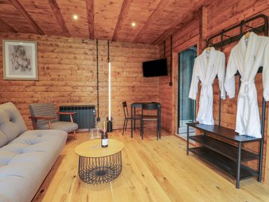 A wooden room with sofa chair coat rack and table with glasses and bottle at Badgers Burrow in South Luffenham near Edith Weston