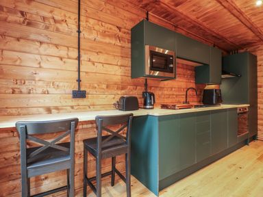 A kitchen with dark cabinets wooden walls two stools microwave toaster kettle and sink at Badger's Burrow South Luffenham near Edith Weston