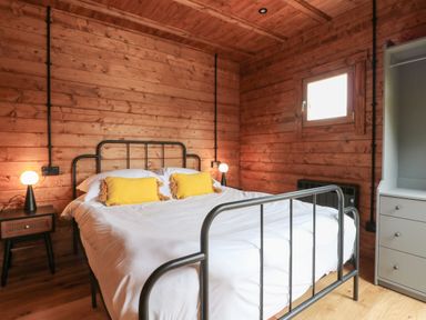 A bedroom with a metal bed frame two yellow pillows white bedding wooden walls and two bedside tables with lamps at Badger's Burrow in South Luffenham near Edith Weston