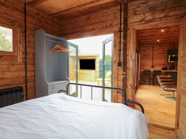 A bedroom with a metal framed bed and an open wardrobe next to glass doors leading to an outdoor area with a wooden TV cover at Badgers Burrow South Luffenham near Edith Weston