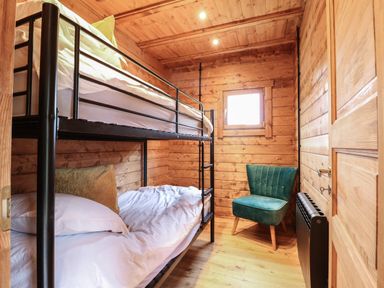 A small wooden bedroom with a black metal bunk bed and a green upholstered chair at Badger's Burrow in South Luffenham near Edith Weston