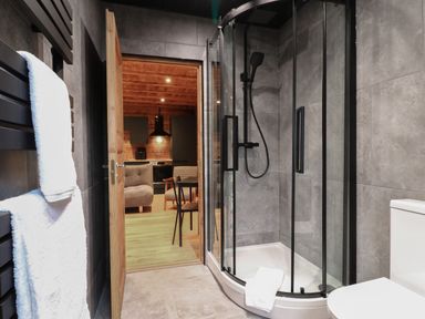 A bathroom with a glass shower enclosure a toilet white towels on a radiator and a door leading to a wooden kitchen area with chairs at Badger's Burrow in South Luffenham near Edith Weston