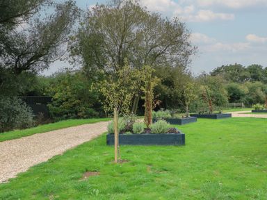 A garden with grass and trees planted in raised beds along a gravel path at Badger's Burrow in South Luffenham near Edith Weston