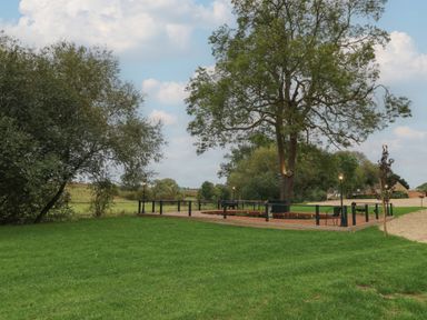 An outdoor seating area with chairs around a tree and lampposts on a green lawn at Badger's Burrow in South Luffenham near Edith Weston