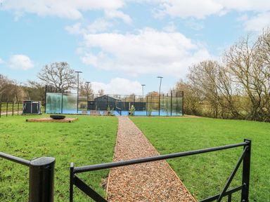 An outdoor area with a pathway and tennis court at Badger's Burrow in Edith Weston