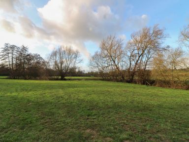 A grassy area with trees and a cloudy sky at Badger's Burrow in Edith Weston