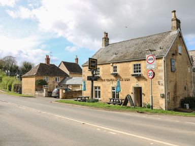 A pub with a sign in front and houses nearby at Badger's Burrow in Edith Weston