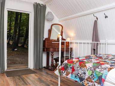 A bedroom with a metal bed frame and a colorful patchwork quilt and a wooden dressing table with a mirror and a lamp at Ballybeg Pod 9 Ballybeg near Tinahely County Wicklow