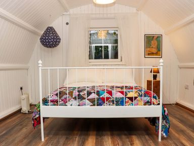 A bedroom with a white metal bed frame covered by a colorful patchwork quilt and a window behind it at Ballybeg Pod 2 Ballybeg near Tinahely County Wicklow