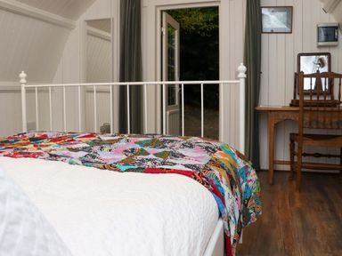 A bedroom with a white metal bed frame a colorful quilt wooden desk and chair and an open door showing outside at Ballybeg Pod 4 Ballybeg near Tinahely County Wicklow