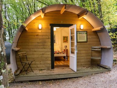 An arched wooden pod with a white door open showing a bed inside and two chairs outside at Ballybeg Pod 5 Ballybeg near Tinahely County Wicklow