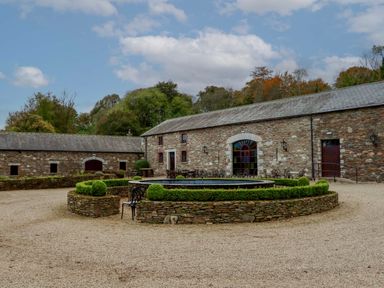 A stone building with arched doorways and windows surrounding a circular stone planter with greenery Ballybeg Pod 8 Ballybeg near Tinahely County Wicklow