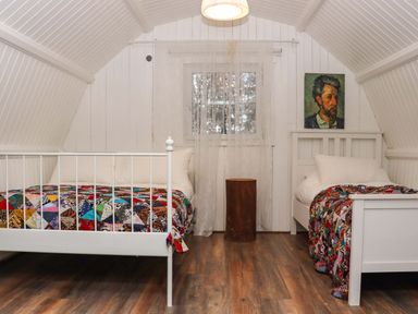 A bedroom with two beds covered with patchwork quilts a wooden stump side table a small window with lace curtains and a portrait painting on the wall at Ballybeg Pod 10 Ballybeg near Tinahely County Wicklow