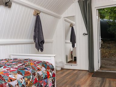 A bedroom with a patchwork quilt on a bed a gray towel hanging on the wall a full-length mirror and an open door leading outside at Ballybeg Pod 10 Ballybeg near Tinahely County Wicklow