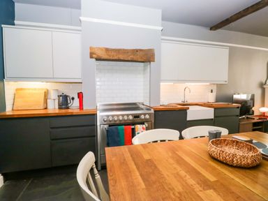 A kitchen with cabinets, countertop, stove, sink, and dining table at Unicorn Cottage