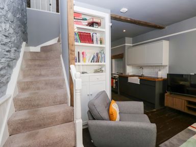 A living room with a staircase and kitchen area at Unicorn Cottage 