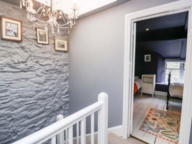A hallway with a chandelier and stone wall at Unicorn Cottage