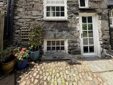 An exterior view showing a stone wall with a door and plants at Unicorn Cottage in Ambleside