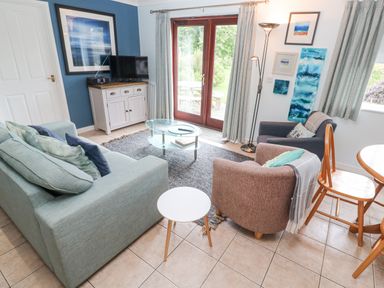 A living room with blue and brown chairs a glass coffee table and a cabinet with a television at Chy Lowena Goldenbank near Budock Water