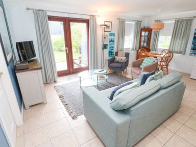 A living room with blue sofa armchairs glass coffee table and wooden dining table with chairs at Chy Lowena Goldenbank near Budock Water